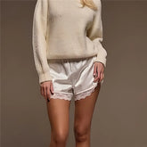 Person wearing a cream sweater and white satin shorts with lace trim on a brown background